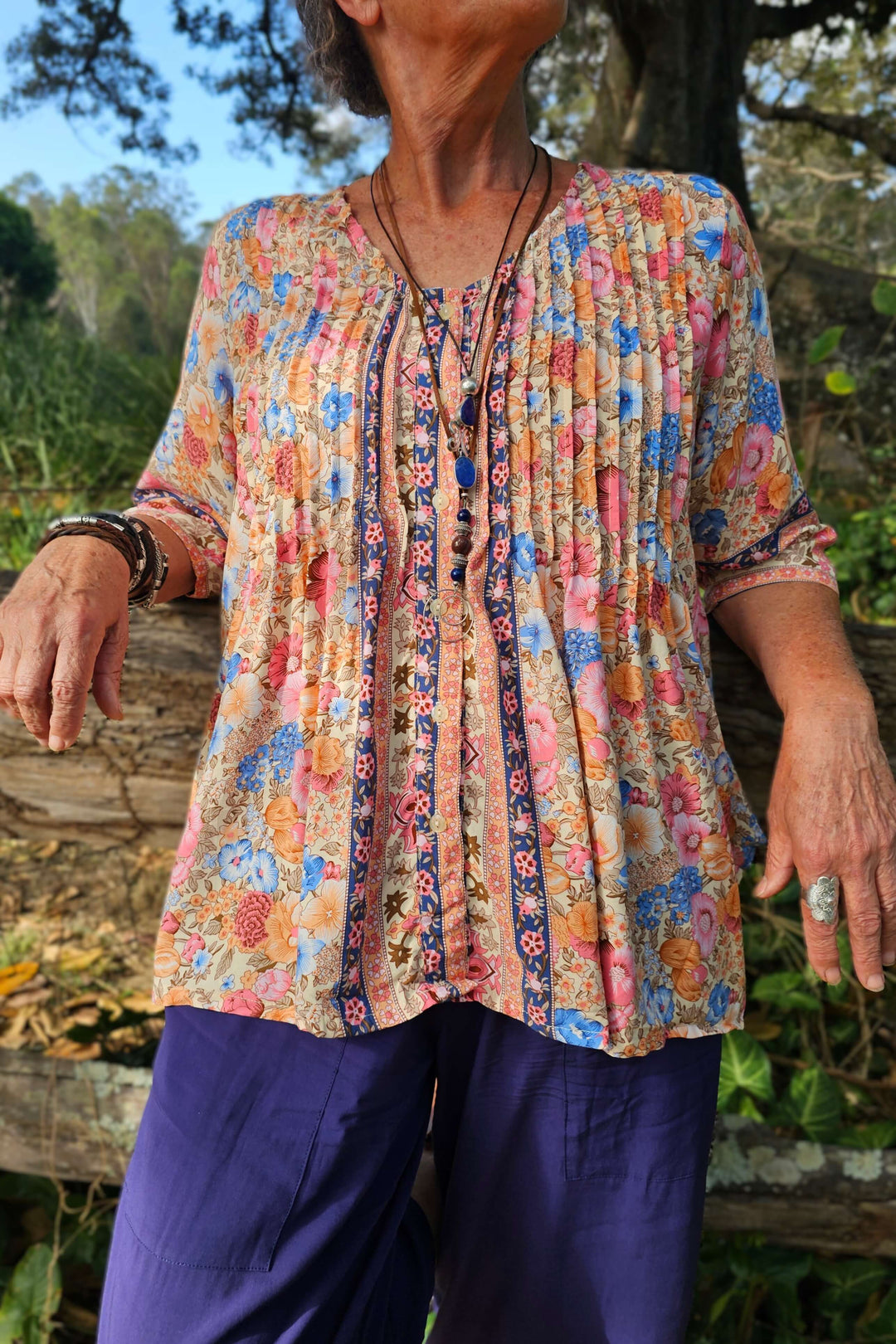 Person wearing a colorful floral blouse and purple pants outdoors.