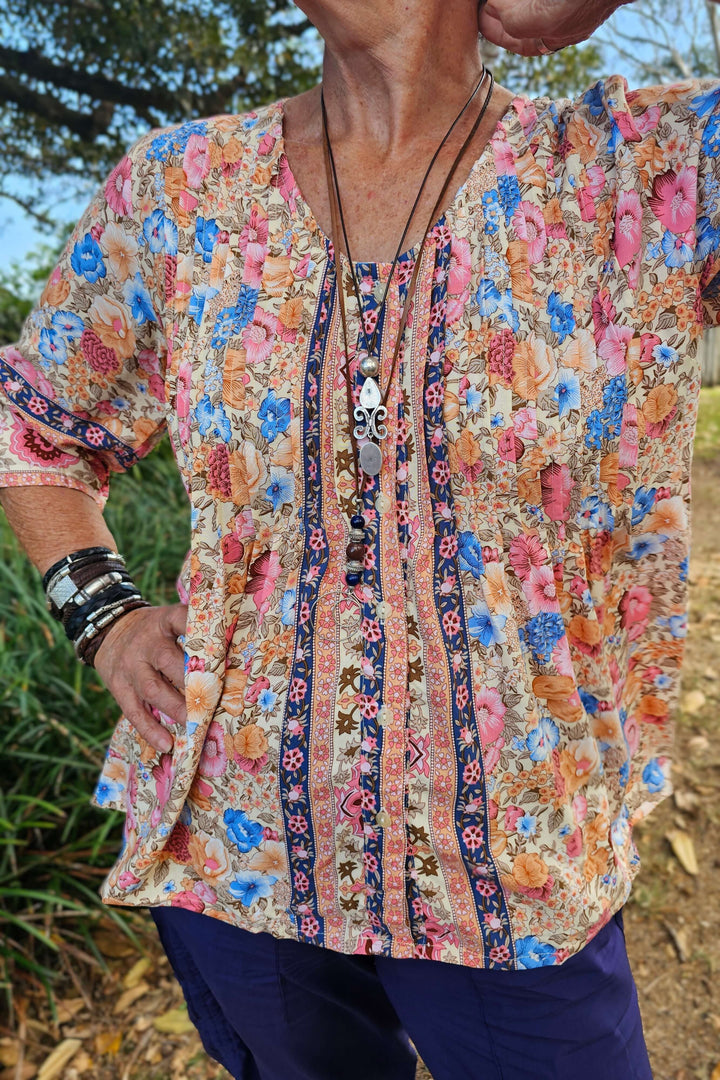 Person wearing a colorful floral blouse with a patterned trim outdoors.