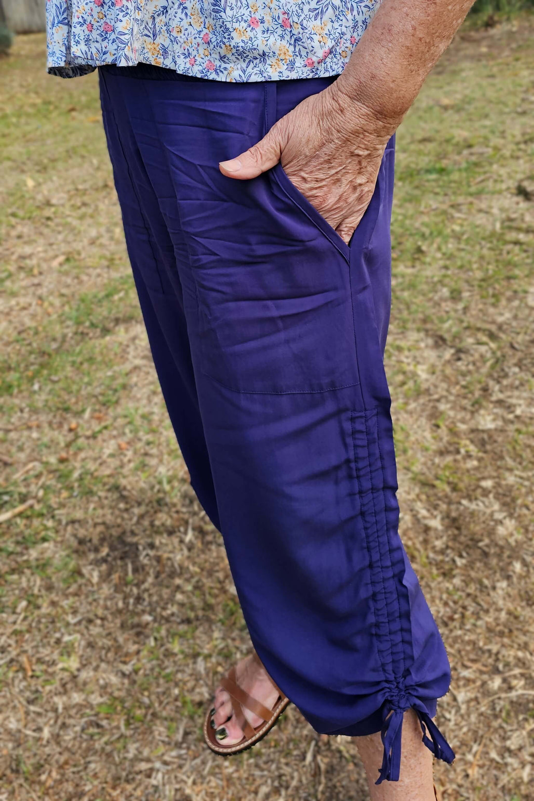 Size 14 women wearing a floral top and navy pants with a tied bottom, with her hand in pocket