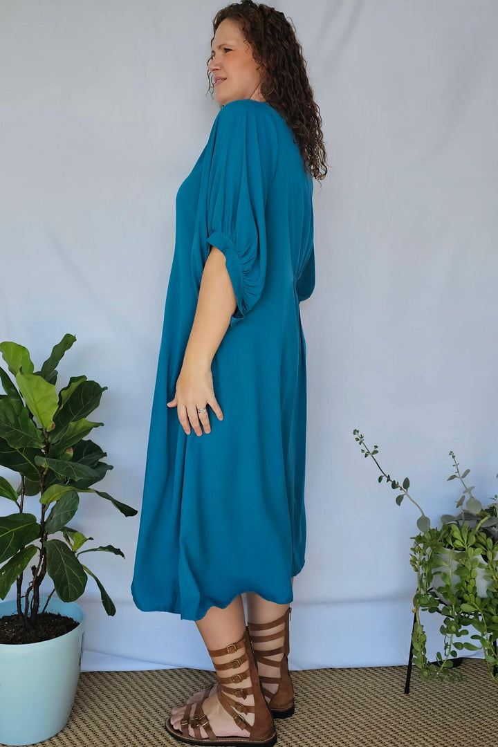 Side angle showing shirred waist and dipped hem of teal rayon dress